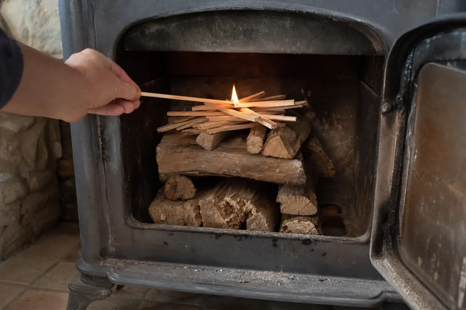 Bûches empilées dans un poêle avec du petit bois au sommet et un allume-feu enflammé