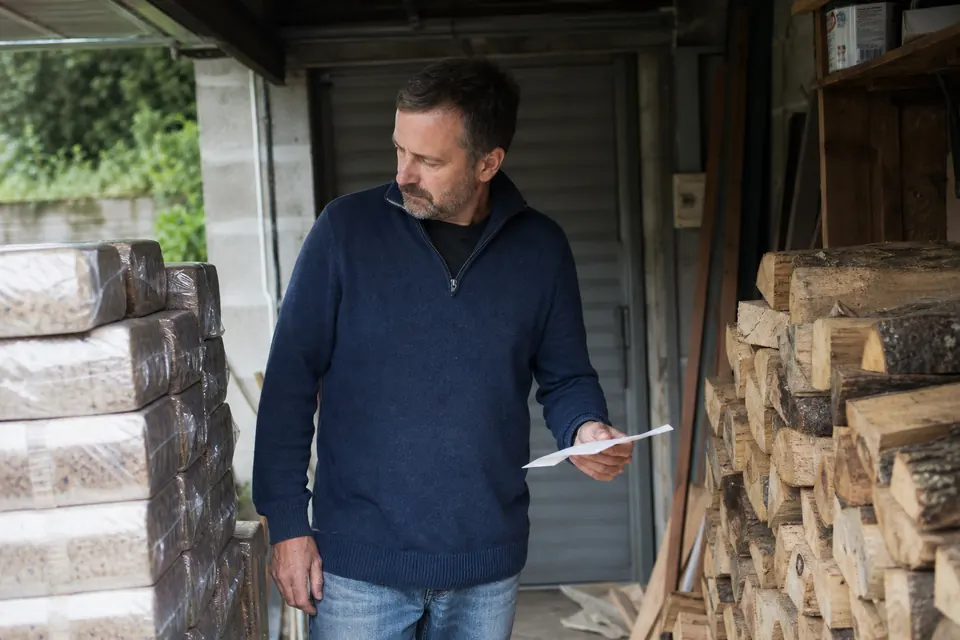 Homme comparant un tas de bûches et des cartons de bûches densifiées dans son garage