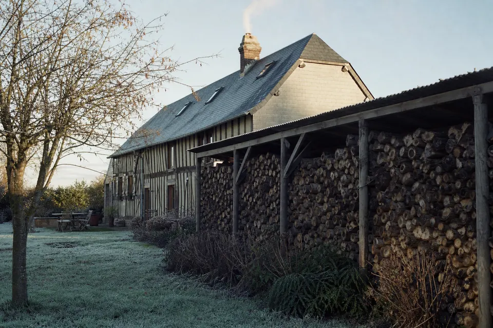 Long tas de bois abrité le long d'une maison normande à colombages un matin de gelée