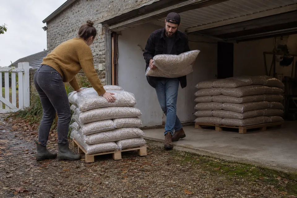 Jeune couple rentrant des sacs de granulés dans un garage depuis une palette livrée