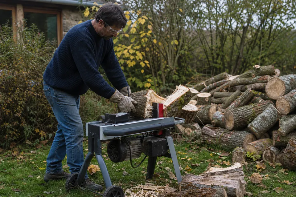 Homme en lunettes de protection utilisant un fendeur de bûches électrique horizontal dans son jardin
