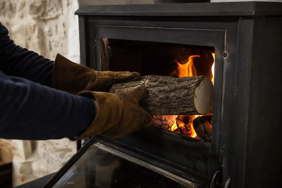 Mains protégées par d'épais gants en cuir plaçant une bûche dans un poêle allumé