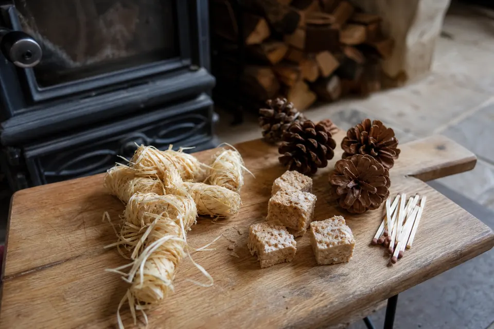 Allume-feu naturels en laine de bois, pommes de pin et cubes posés sur une planche près d'un poêle