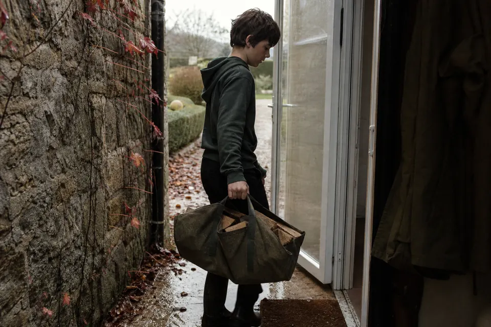 Adolescent portant un sac de toile rempli de bûches à travers la porte arrière d'une maison
