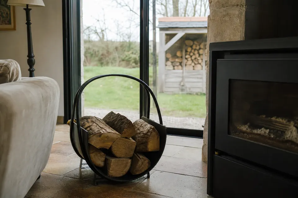 Range-bûches métallique rempli près d'un poêle moderne, abri à bois visible dans le jardin