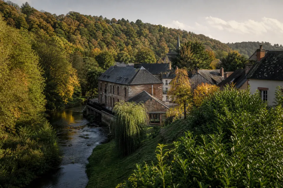 Ancien moulin en briques au bord d'une rivière, dans une vallée étroite bordée de coteaux boisés