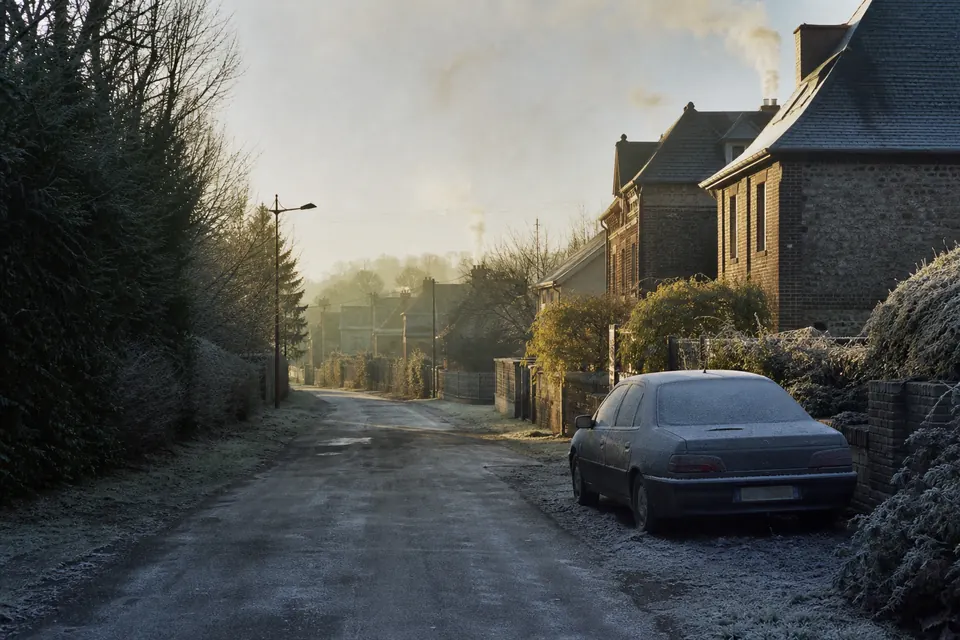 Rue de village un matin de gelée, fumée des cheminées et voiture givrée